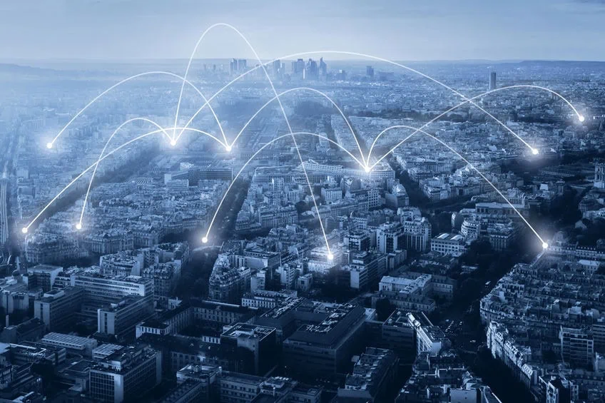 Vue aérienne d'une ville avec des lignes numériques blanches et des points illustrant la connectivité du réseau, montrant comment une agence de communication ou un travailleur autonome peut rester connecté à différents endroits.